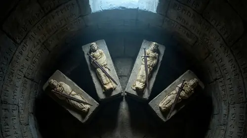 Four small figures lying on stone slabs in a barrow, dressed in white with gold crowns, pale and still as death, a single long sword laid across their necks, treasures scattered around them, one pale…
