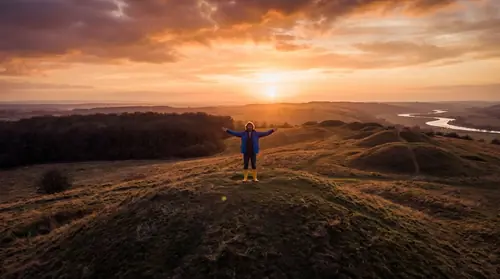Tom Bombadil standing on a hilltop at sunset, his domain visible around him—the Old Forest and Barrow-downs, vast but bounded, his expression enigmatic and timeless